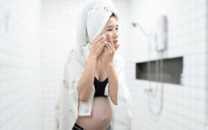Pregnant asian woman checking her skin in bathroom mirror