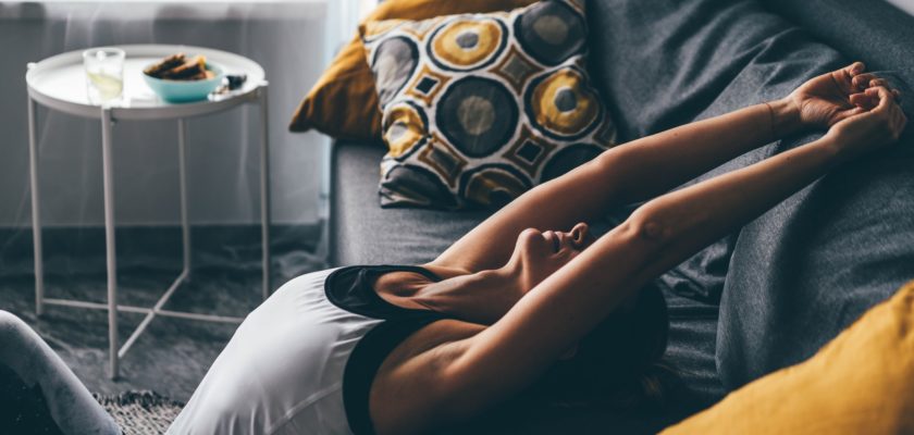 Blonde woman stretches back leaning on sofa and practising yoga