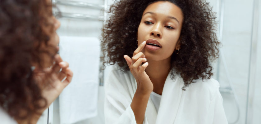 Woman applying Elixir Mind Body Botanicals Lip Balm to her lips in mirror