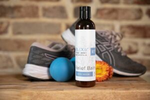 Elixir Mind Body Botanicals Relief Balm next to RAD Roller and running shoes