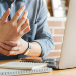 man rubbing his wrist at computer because he has carpal tunnel syndrome